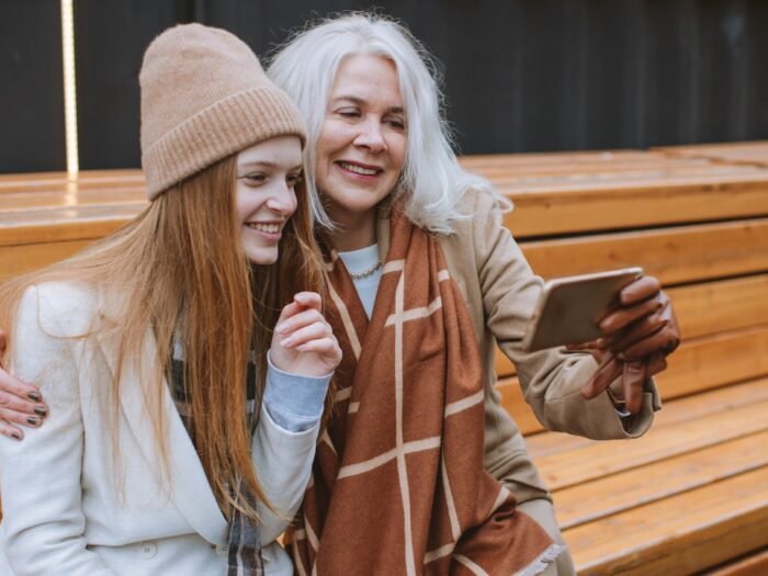 women sitting on a bench taking a selfie with a smartphone