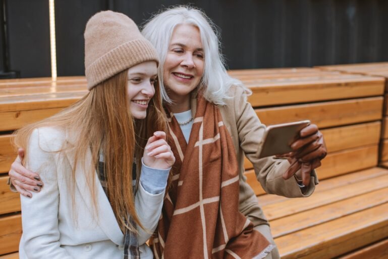 women sitting on a bench taking a selfie with a smartphone