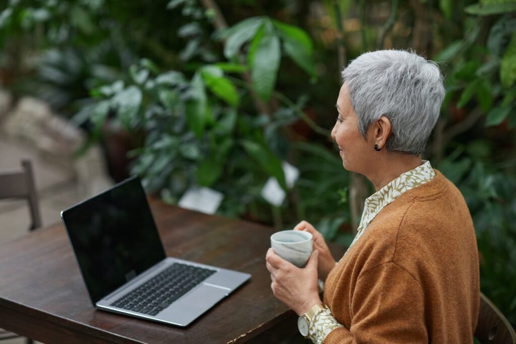 Woman drinking coffee at a table outside with her laptop open.