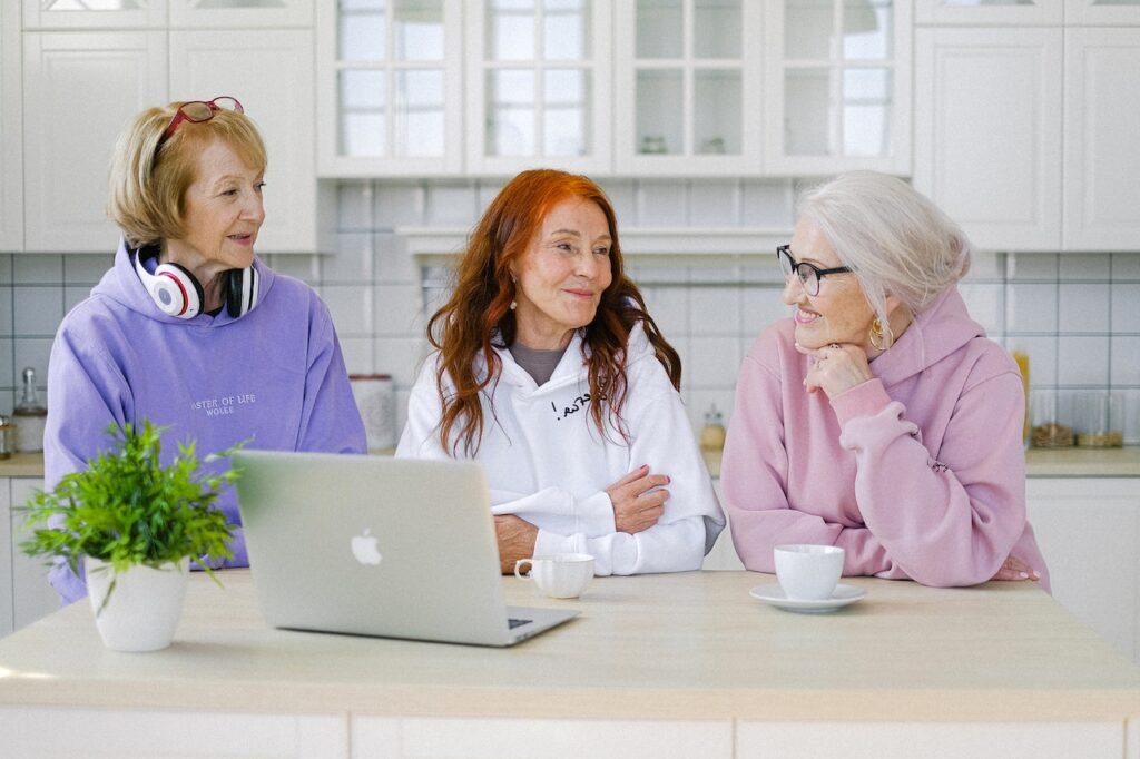 Three woman sitting at a counter with a laptop chatting over coffee.