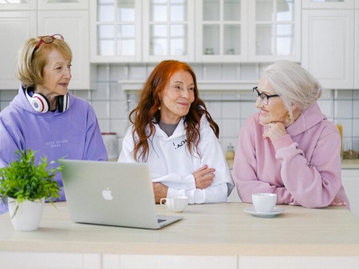 Three woman sitting at a counter with a laptop chatting over coffee.