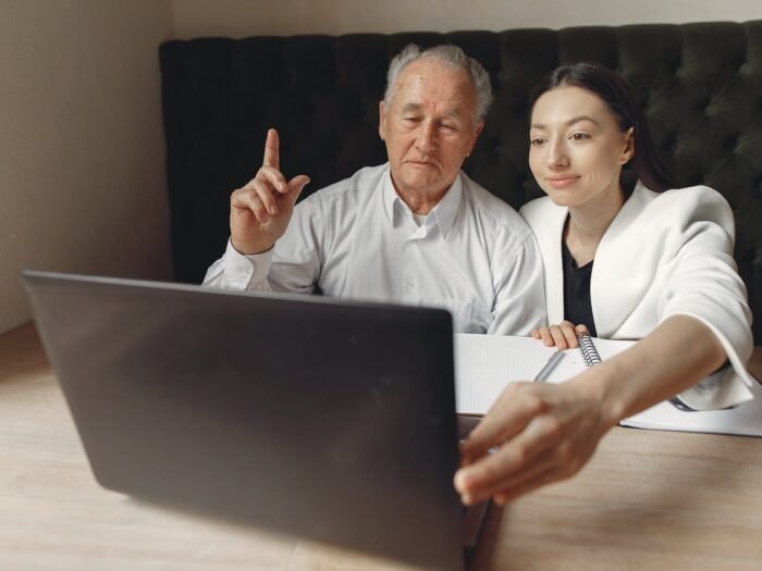 older man and younger woman talking and using a laptop computer