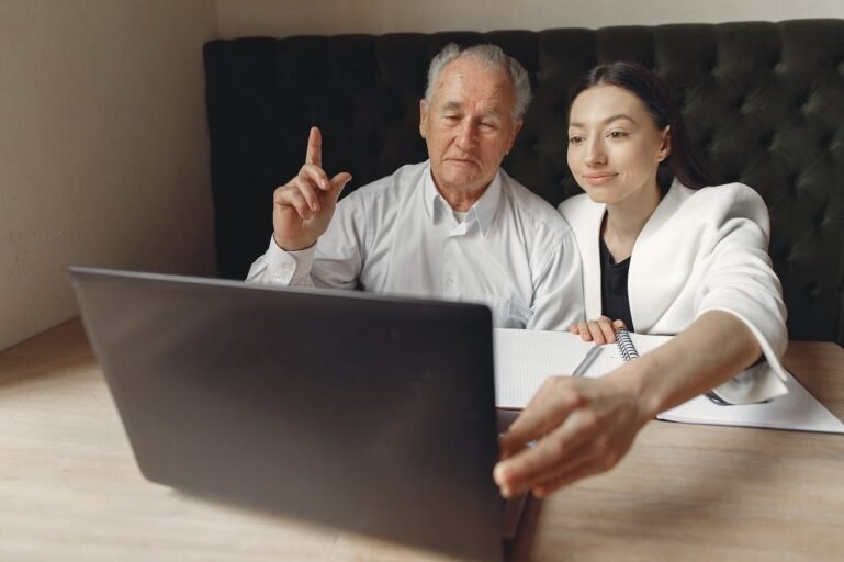 older man and younger woman talking and using a laptop computer